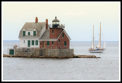 saiboat passes by Rockland Breakwater lighthouse n a cloudy day